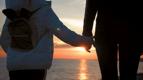 Silhouette of Mothers and Daughters Walking on the Beach While Holding Hands with Sunset Background
