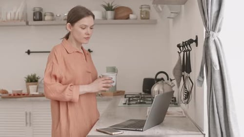 Woman Works on Laptop with Coffee in Kitchen