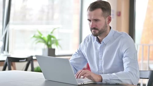 Serious Young Man Working on Laptop in Office