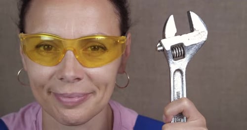 Smiling Woman Holding Adjustable Wrench, Wearing Safety Glasses