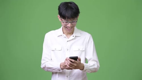 Young Man Smiling Using Smartphone on Green Background