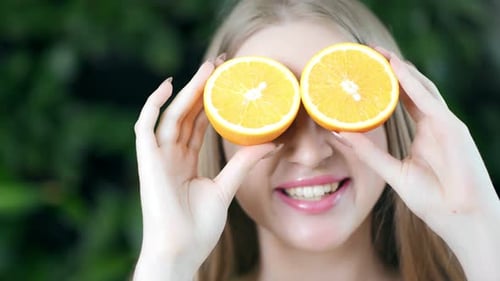 Smiling Woman Holding Orange Slices Over Her Eyes