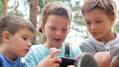 Three Boys Watching a Smartphone Together Outdoors