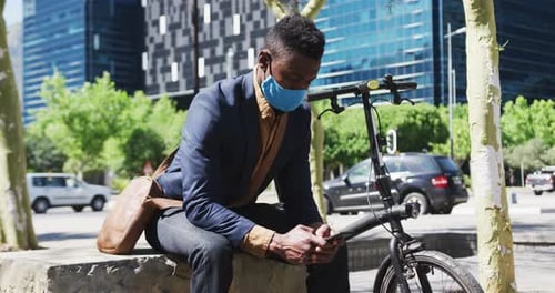 African american businessman wearing face mask texting on smartphone in street