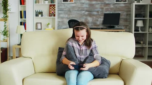 Girl Happily Playing Game on Smartphone on Couch