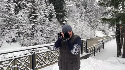 Man Photographer Shoots Snowcovered Trees and a Mountain River