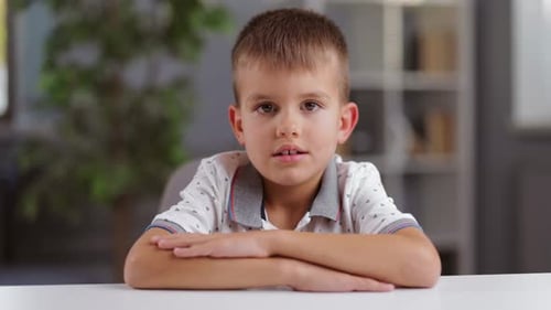 Young Boy Sits at a Table, Arms Crossed