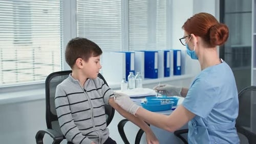 Hospital Office Masked Doctor in Blue Uniform and Protective Gloves Giving an Injection to Little