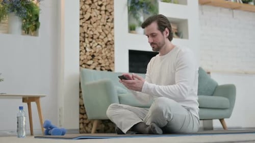 Man Sitting on Yoga Mat Using Smartphone