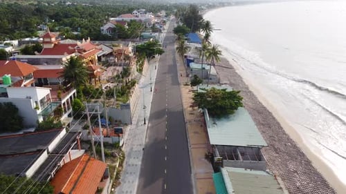 Main empty street of coastal Vietnamese town, passing by temple, aerial ascend view