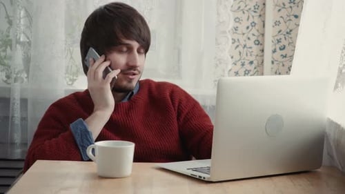 Young Male Freelancer Chatting on Mobile Phone While Sitting Front Open Laptop Computer Cafe