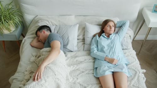 Trauriges Mädchen im Pyjama liegt seufzend im Bett, während der Freund zu Hause schläft