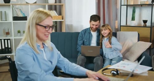 Mujer discapacitada trabajando en una computadora portátil en casa y saludando a su cariñoso esposo barbudo
