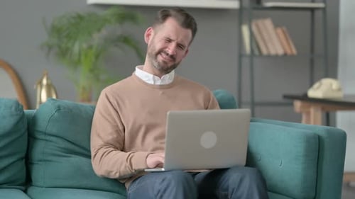 Man Rubbing Neck While Using Laptop at Home