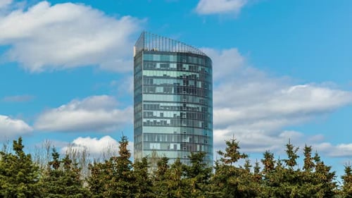 the glass building rises above the trees. modern construction near the street, futuristic building