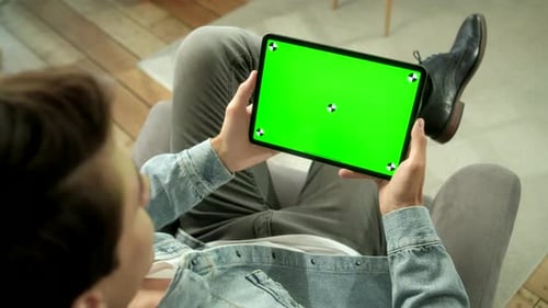 View From the Shoulder of Man Holding and Using Hand Gestures on Green Mock-up Screen Digital Tablet
