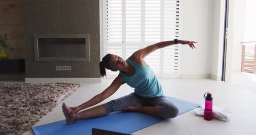 Mixed race woman excercising on a mat with laptop