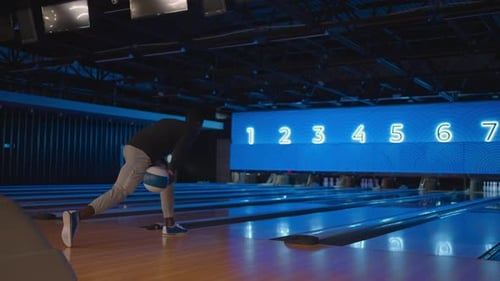 Ein schwarzer Bowlingmann wirft einen Ball in Zeitlupe und schlägt Kegeln nieder