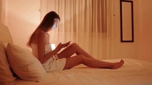 Woman Using Phone Relaxing on Bed at Night