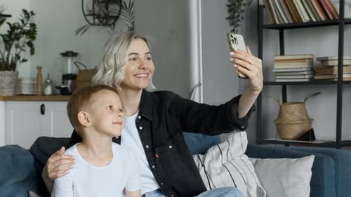 Close up of happy smiling young beautiful mom sitting on sofa with cute little son making gestures