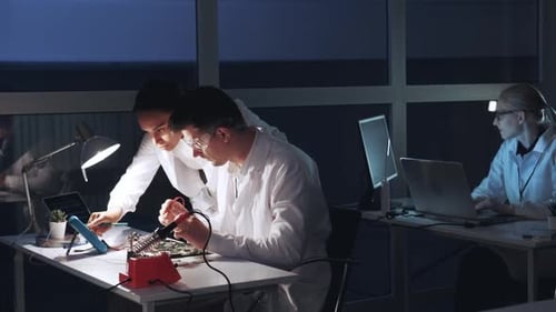 Hombre y mujer multirraciales comprobando la placa base con el multímetro en el laboratorio de electrónica