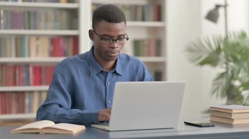 Young Adult Smiling While Typing on Laptop
