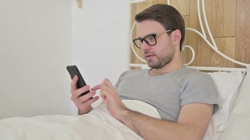Man Using Smart Phone in Bed