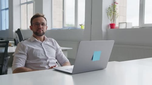 Homem sentado olha para a tela do computador e para a câmera