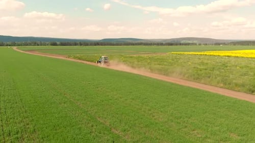 Drone Flying Over Field and Blue Cultivation Tractor Driving on a Ground Road.