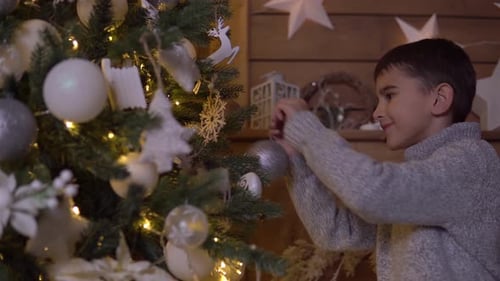 Boy Decorates Christmas Tree With Silver Ornaments at Home