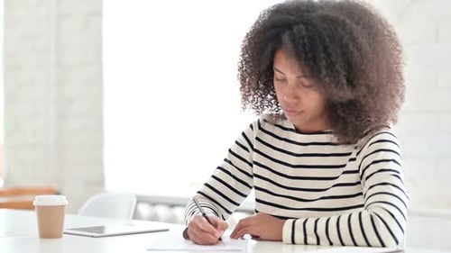 Young Woman Writing at Desk in Bright Office