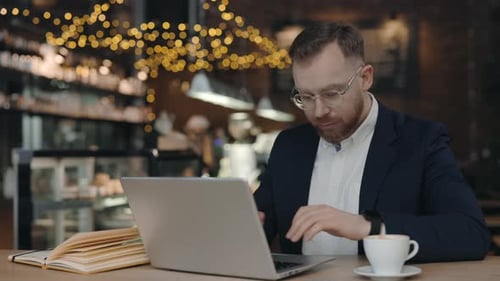 Businessman Drinking and Typing at Keyboard While Working at Computer in Cafe