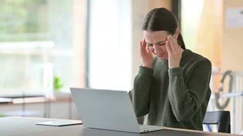 Woman Massages Temples While Using Laptop