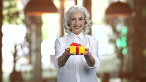 Senior Woman Holds Yellow Gift Box Smiling