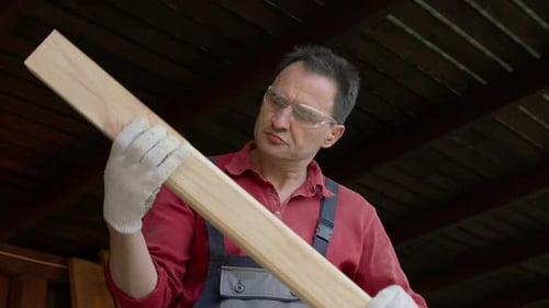 Man Inspecting Wooden Plank in Workshop