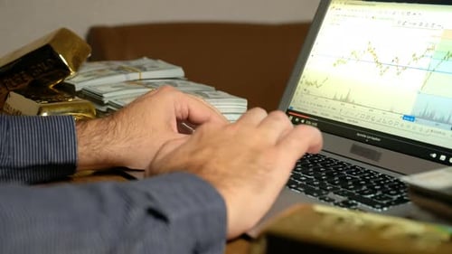 Hands Typing on Laptop with Gold and Money