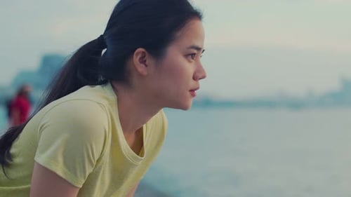 Asian female athlete taking rest after fitness running at the beach.
