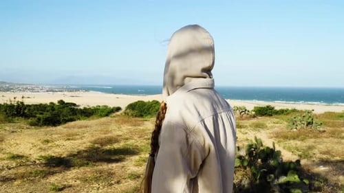 Close up shot of Woman wearing hoodie during windy day and watching beautiful sand dunes and Ocean o