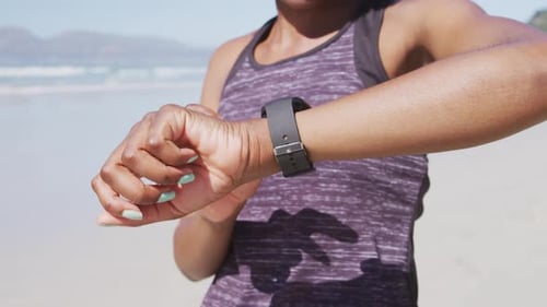 Mixed race woman looking at her smartwatch on the beach and blue sky background