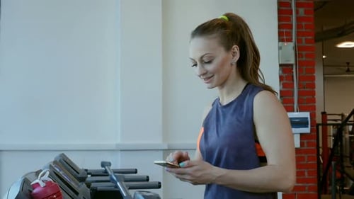 Woman Uses Phone Next to Treadmill in Gym