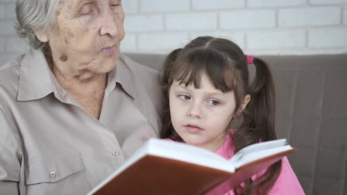 Grandmother Reading Book With Little Girl on Couch