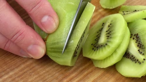 Hand Slicing Fresh Kiwi Fruit on Wood Board