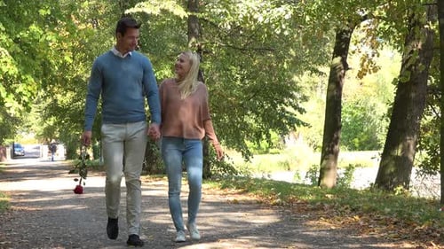 A Young Attractive Couple Talks and Strolls Down a Pathway Through a Park on a Sunny Day