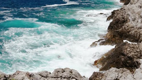 Sea Waves Breaking Against the Rocky Shore. Sea Foam on a Sunny Summer Day. Deep Blue Sea Waves Hit