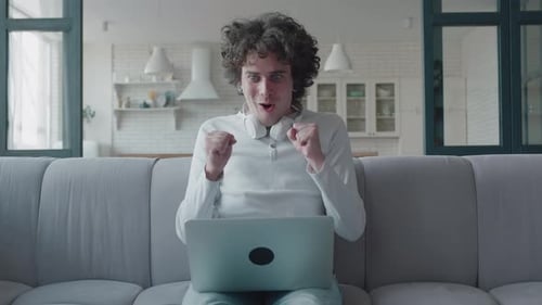 Young Adult Celebrates Laptop Success on Couch