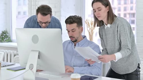Three Colleagues Collaborating on Computer in Modern Office