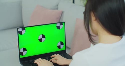 Mixed Race Ethnic Woman Lying on Sofa at Home Uses Laptop with Green Mockup Screen