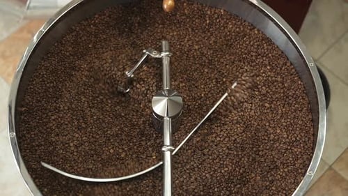 Draufsicht des Mischens gerösteter Kaffeebohnen in professioneller Ausrüstung. Langsam