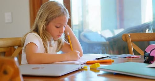 Girl Writes in Notebook at Table Indoors