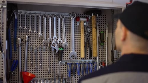 Ein Automechaniker steht in der Nähe des Ständers mit Schraubenschlüsseln und nimmt die erforderliche Größe in Zeitlupe auf